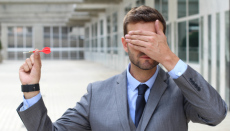 IT budgeting process. A man with his eyes closed holds a dart as if to throw it