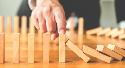 Difference between Disaster Recovery and Business Continuity. A business person stops the collapse of dominoes by preventing one from falling.