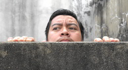 Security posture. A man peeks over a wall, looking with suspicion at something off camera.